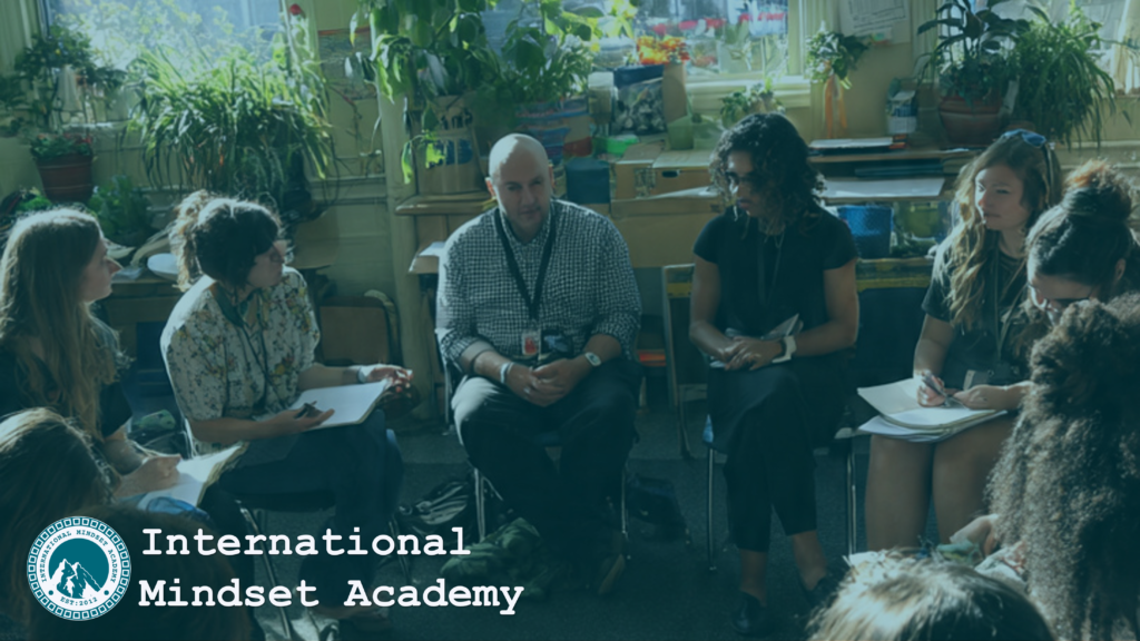 A positive, holistic education session where adults and young learners explore how to heal negative learning patterns through experiential learning and whole person development, seated in a comfortable circle with notebooks, plants, and natural light in a calm classroom, guided by a facilitator who encourages emotional reflection, social connection, and values based dialogue as part of holistic education, creating a psychologically safe and inclusive environment that supports deep mindset transformation and integrated growth. 